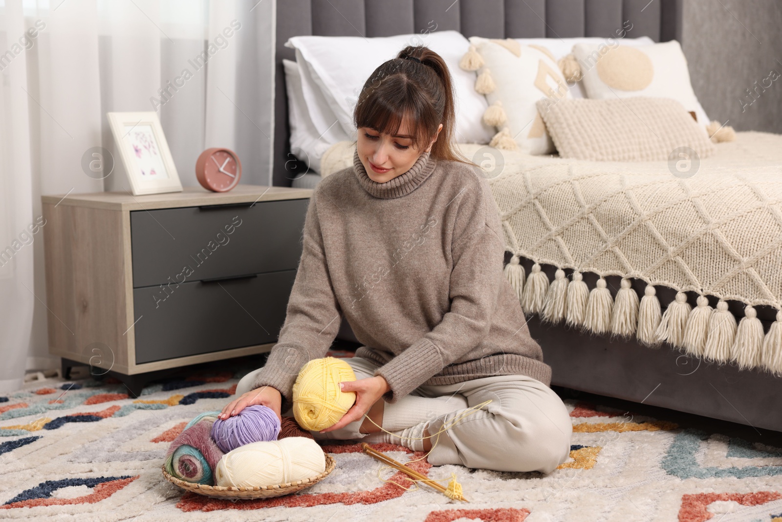 Photo of Beautiful woman with colorful yarns and knitting needles on floor at home