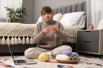 Photo of Woman learning to knit with online course on floor at home