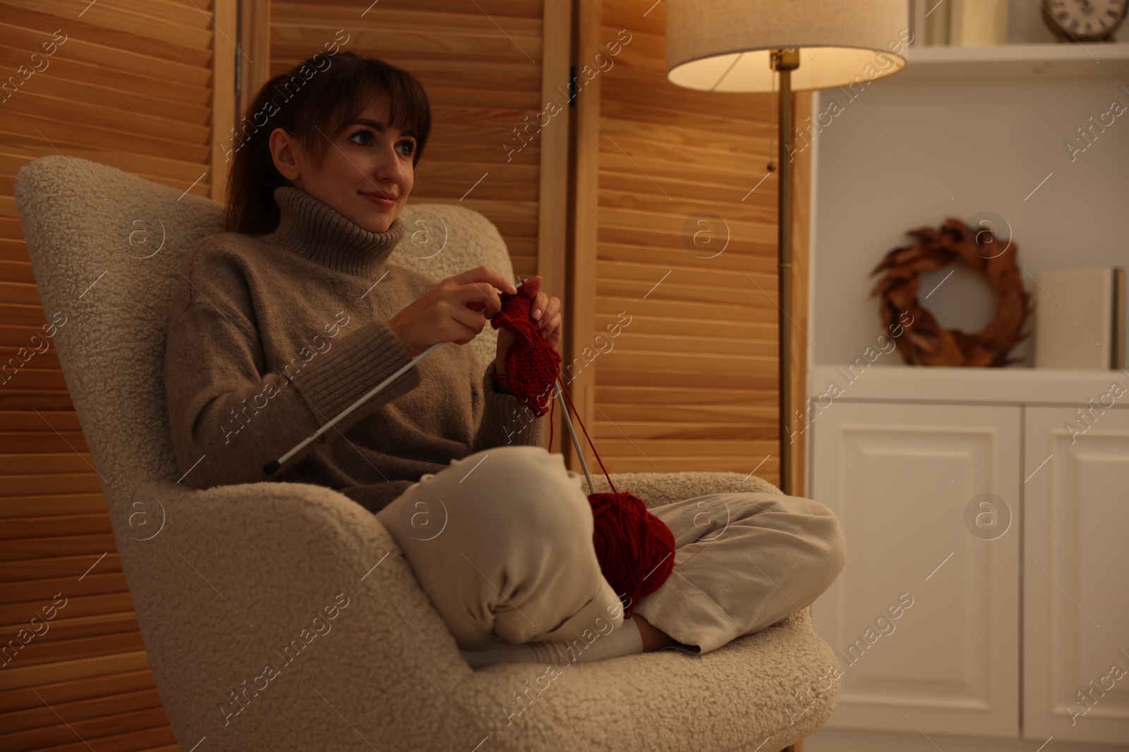 Photo of Beautiful woman knitting with needles in armchair at home