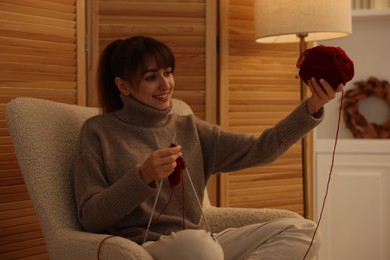 Beautiful woman knitting with needles in armchair at home