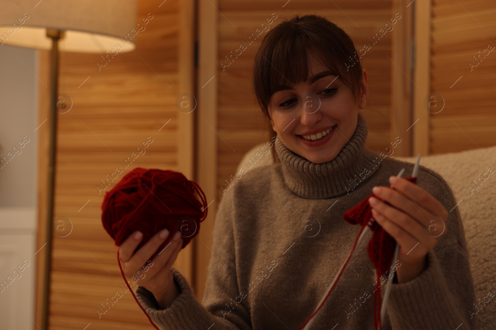 Photo of Beautiful woman knitting with needles in armchair at home