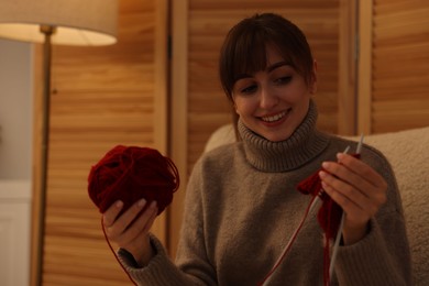 Beautiful woman knitting with needles in armchair at home