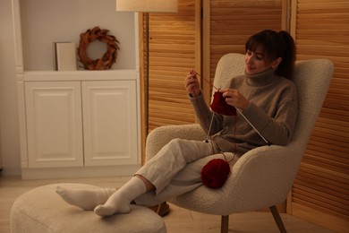 Beautiful woman knitting with needles in armchair at home