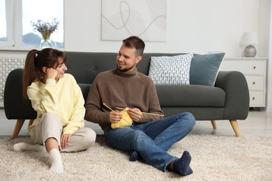 Photo of Woman teaching her boyfriend how to knit on floor at home