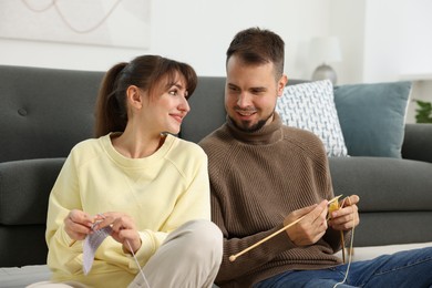 Woman teaching her boyfriend how to knit on floor at home