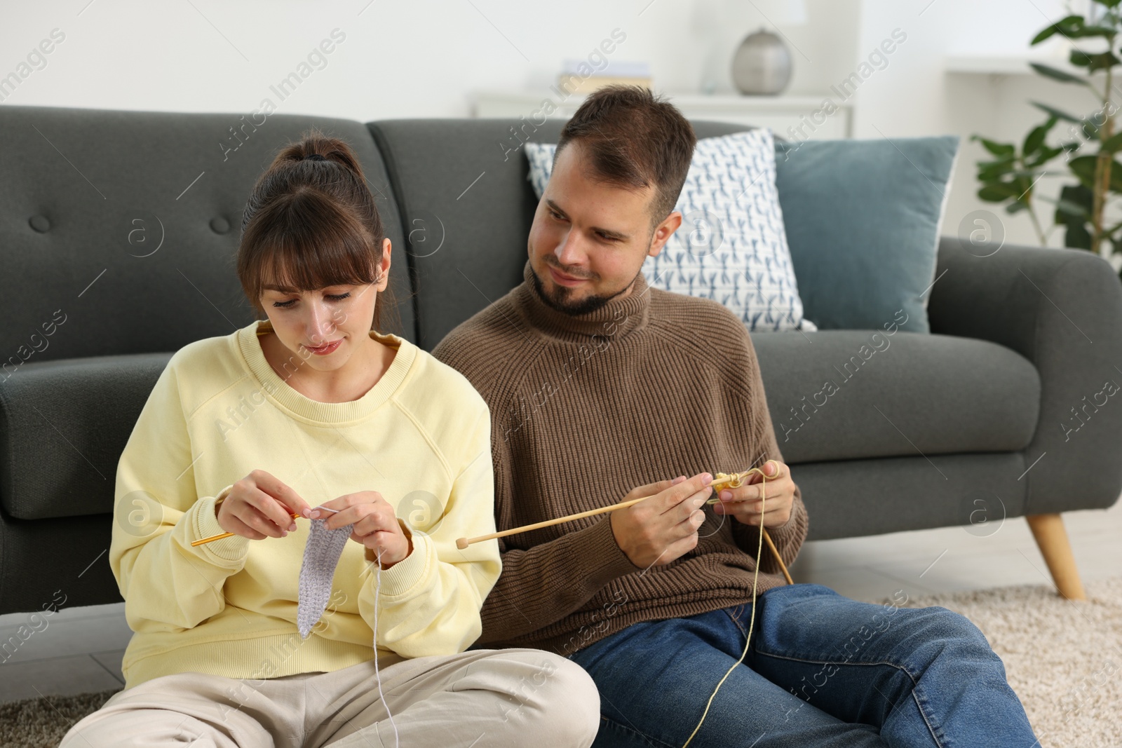 Photo of Woman teaching her boyfriend how to knit on floor at home