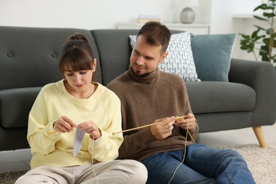 Woman teaching her boyfriend how to knit on floor at home