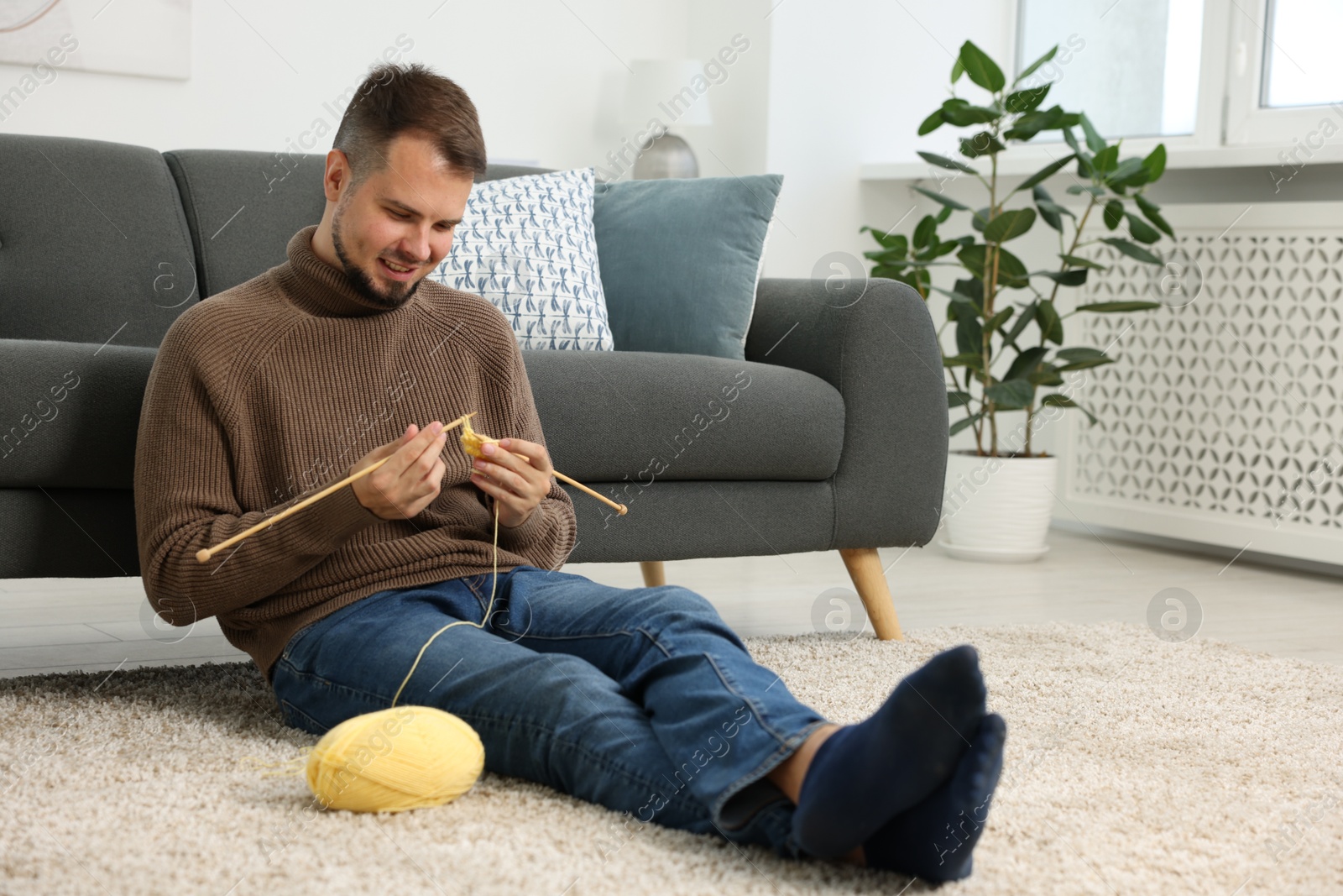 Photo of Man knitting with needles on floor at home