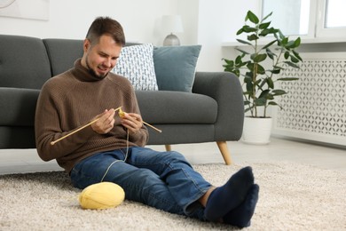 Photo of Man knitting with needles on floor at home