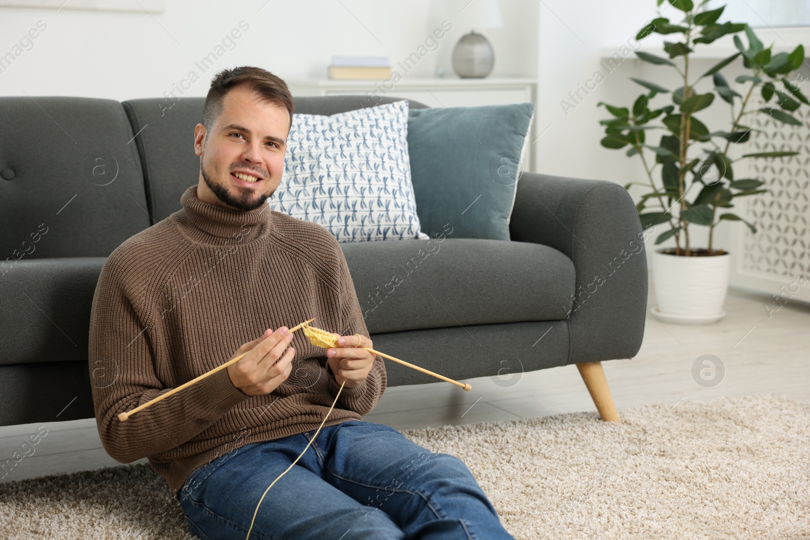 Photo of Man knitting with needles on floor at home