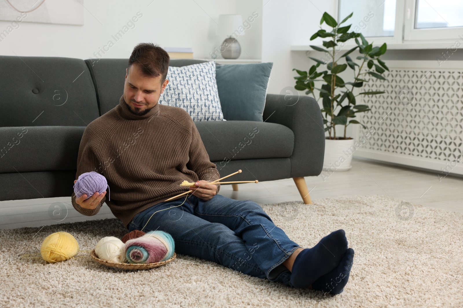 Photo of Man with colorful yarns and knitting needles on floor at home