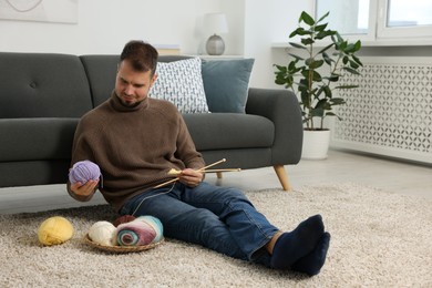 Man with colorful yarns and knitting needles on floor at home