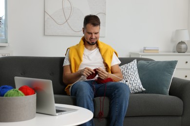 Man learning to knit with online course on sofa at home