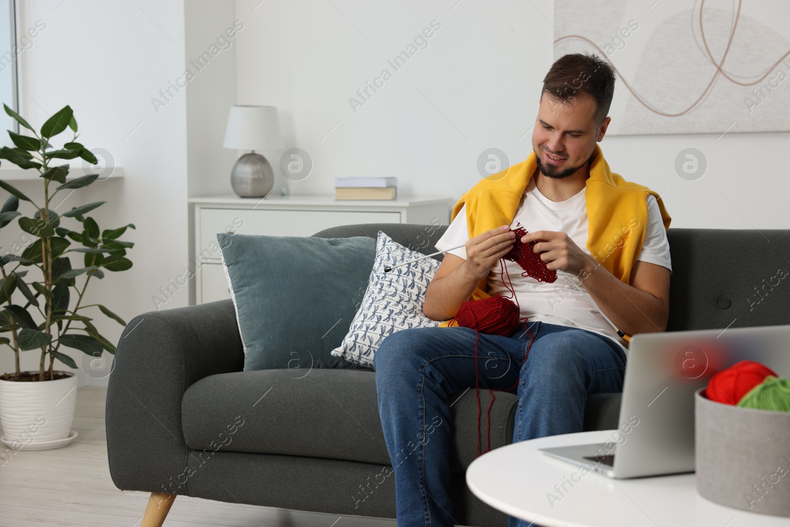 Photo of Man learning to knit with online course on sofa at home