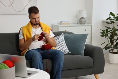 Man learning to knit with online course on sofa at home