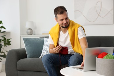 Man learning to knit with online course on sofa at home