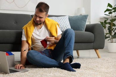 Man learning to knit with online course on floor at home