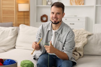 Man knitting with needles on sofa at home