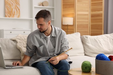 Photo of Man learning to knit with online course on sofa at home