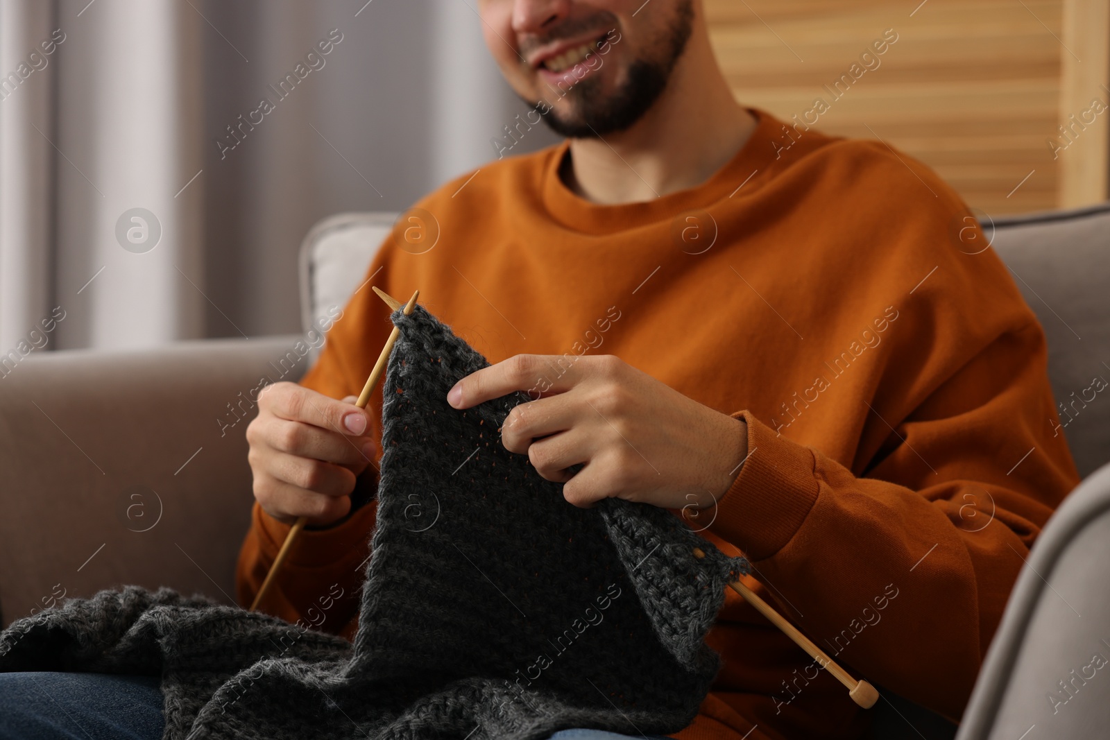 Photo of Man knitting with needles in armchair at home, closeup