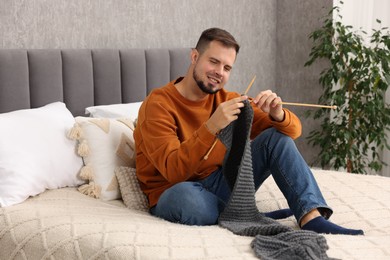 Photo of Man knitting with needles on bed at home