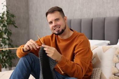 Man knitting with needles on bed at home