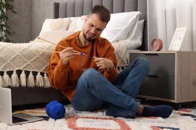 Man learning to knit with online course on floor at home