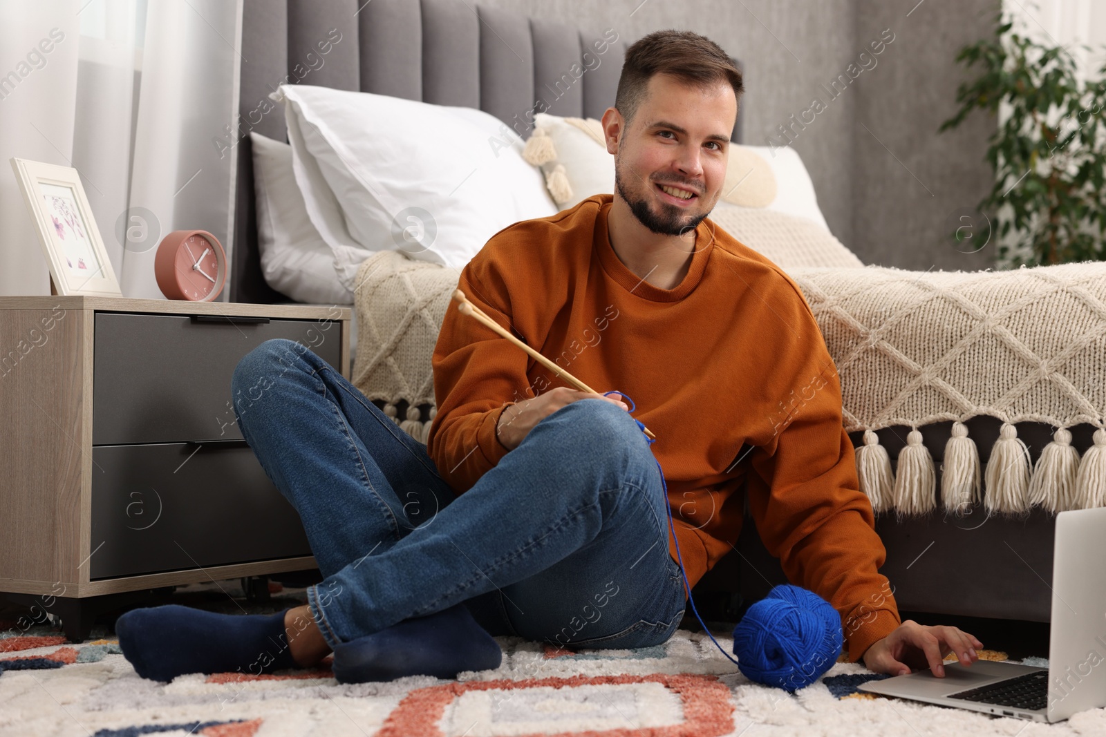 Photo of Man learning to knit with online course on floor at home