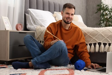 Man learning to knit with online course on floor at home