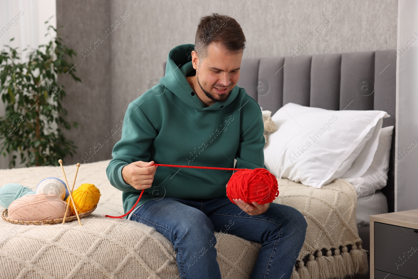 Photo of Man with red yarn on bed at home. Knitting material