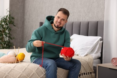 Man with red yarn on bed at home. Knitting material