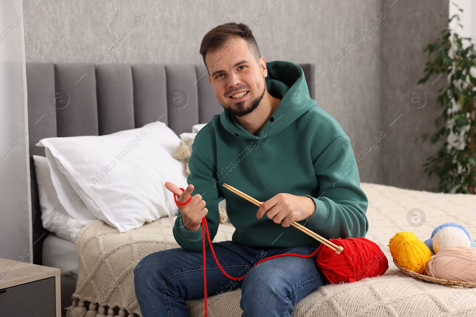 Photo of Man with colorful yarns and knitting needles on bed at home