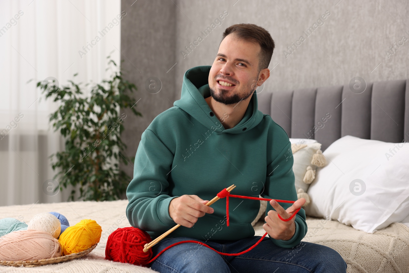 Photo of Man knitting with needles on bed at home