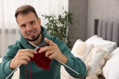 Happy man knitting with needles at home