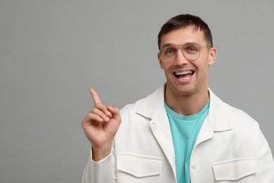 Photo of Happy man with dental braces pointing at something on grey background. Space for text