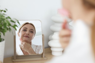 Beautiful woman doing facial self massage with roller near mirror at home