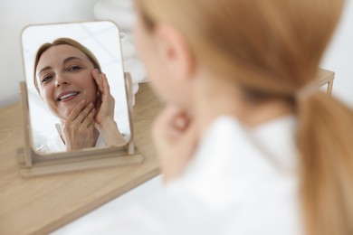 Smiling woman doing facial self massage near mirror at home