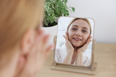 Smiling woman doing facial self massage near mirror at home