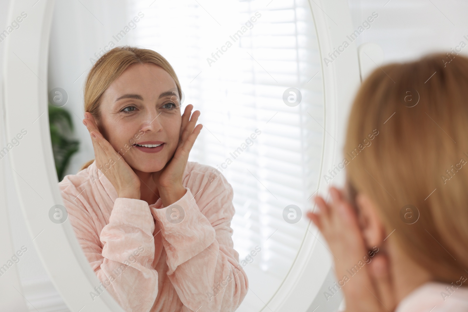 Photo of Smiling woman doing facial self massage near mirror in bathroom