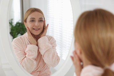 Photo of Smiling woman doing facial self massage near mirror in bathroom