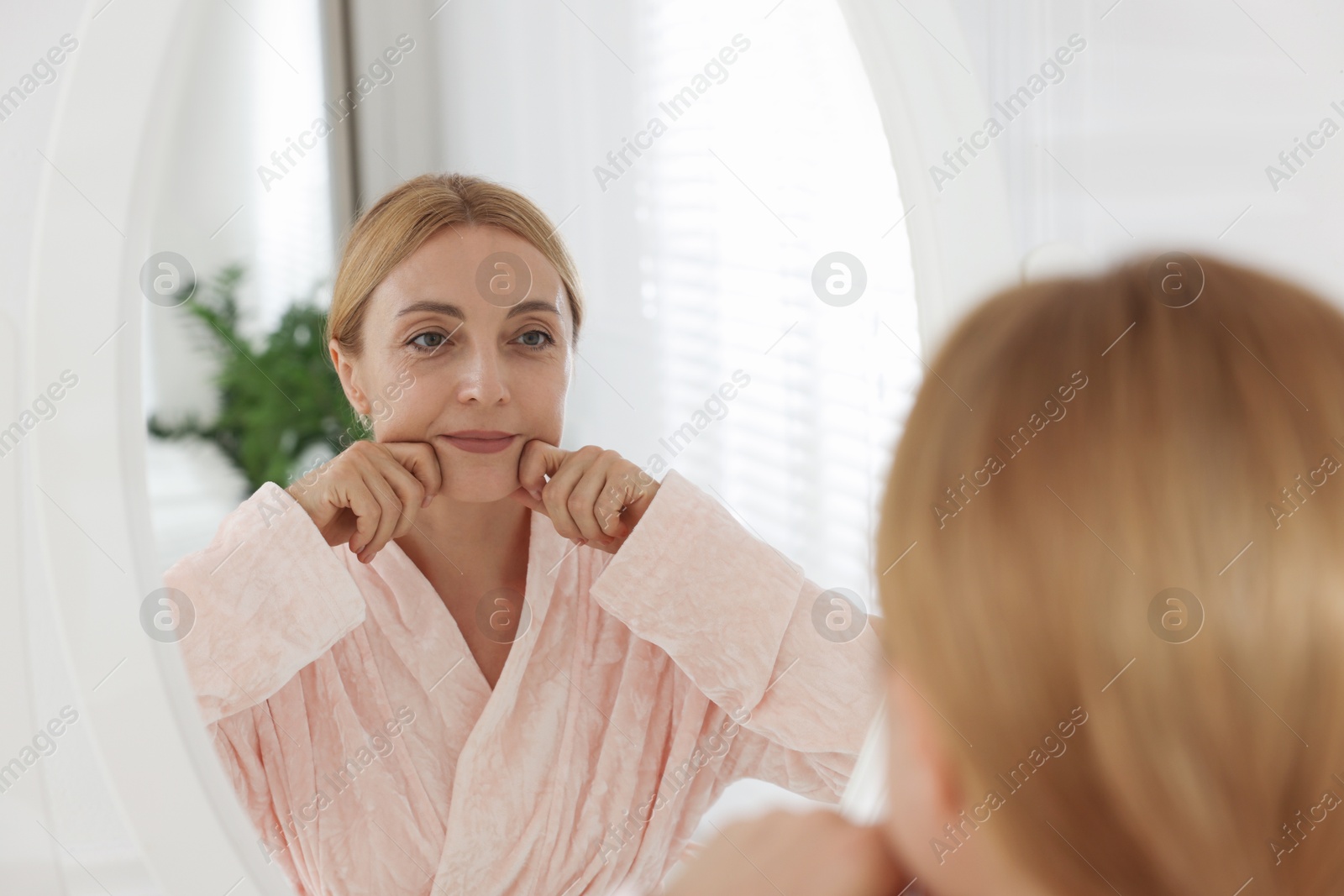 Photo of Beautiful woman doing facial self massage near mirror in bathroom