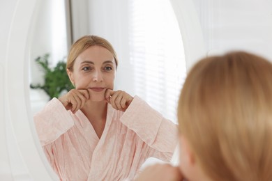 Beautiful woman doing facial self massage near mirror in bathroom