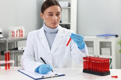 Laboratory testing. Doctor with blood sample taking notes at table indoors