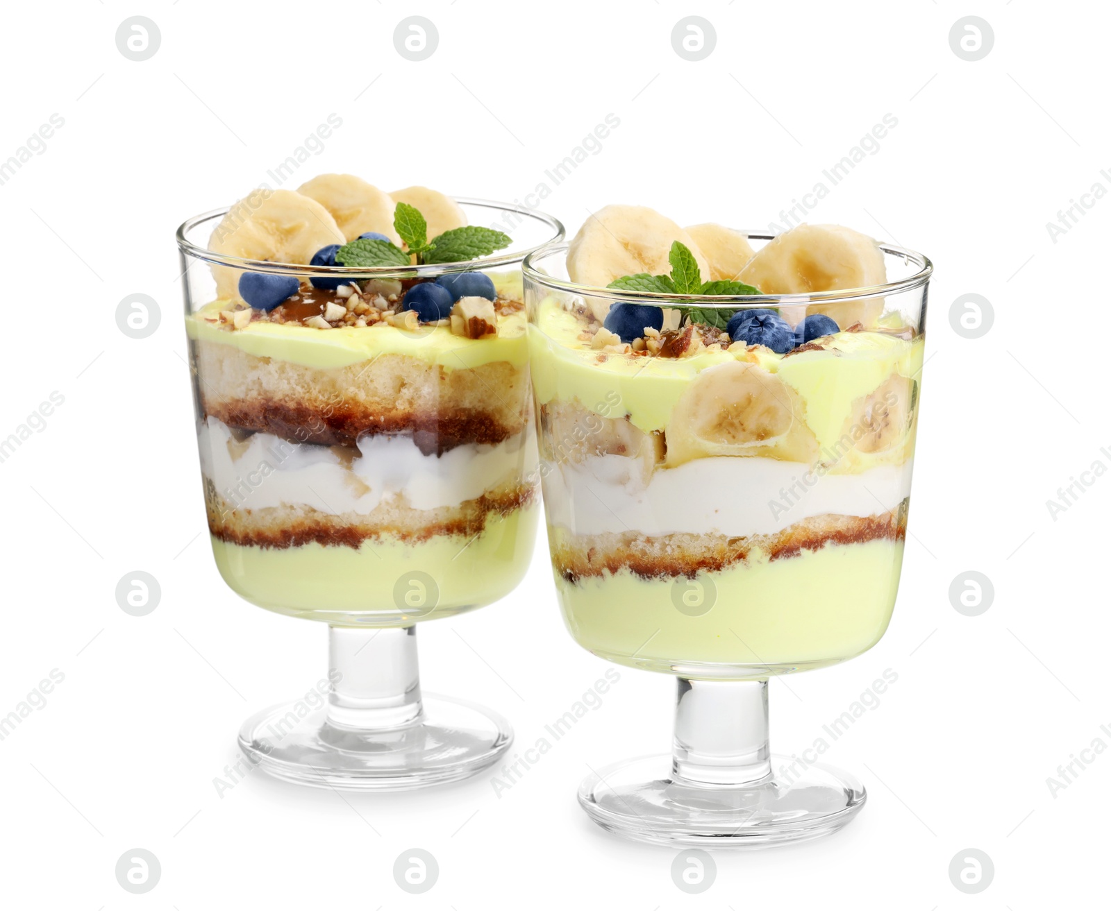 Photo of Tasty trifle dessert. Banana, blueberries, sponge cake and whipped cream in glasses isolated on white