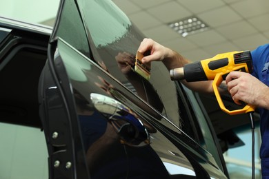 Worker tinting car window with heat gun in workshop, closeup