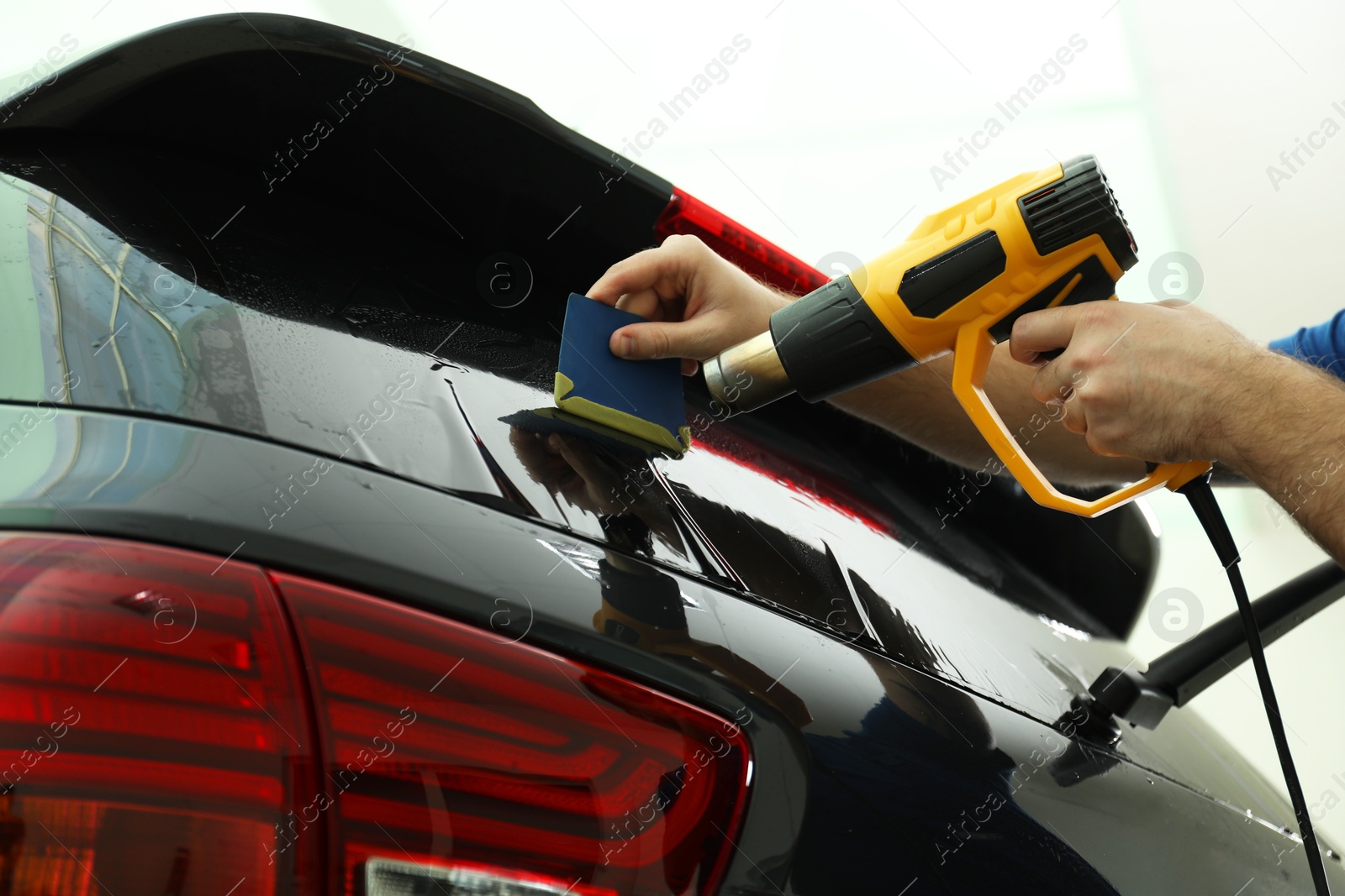 Photo of Worker tinting car window with heat gun in workshop, closeup