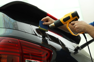 Worker tinting car window with heat gun in workshop, closeup