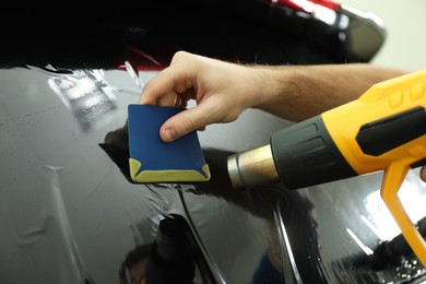 Worker tinting car window with heat gun in workshop, closeup