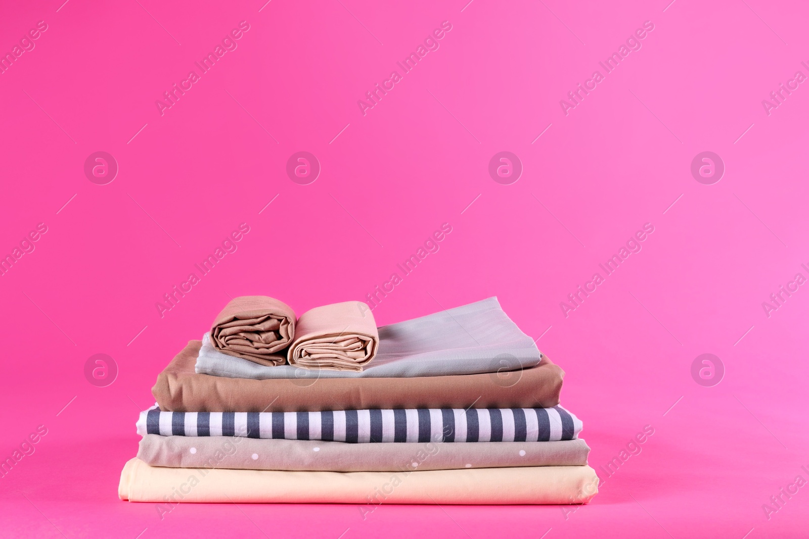 Photo of Stack of clean bed sheets on pink background. Space for text