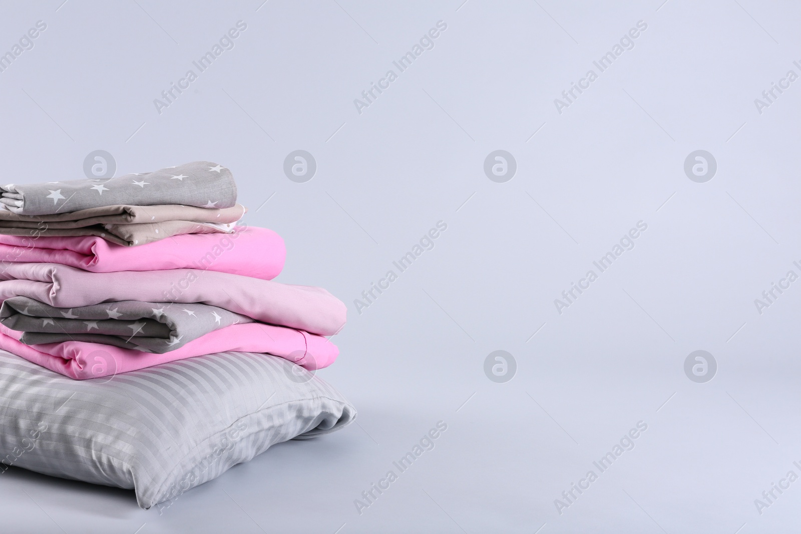 Photo of Stack of clean bed sheets and pillow on white background. Space for text